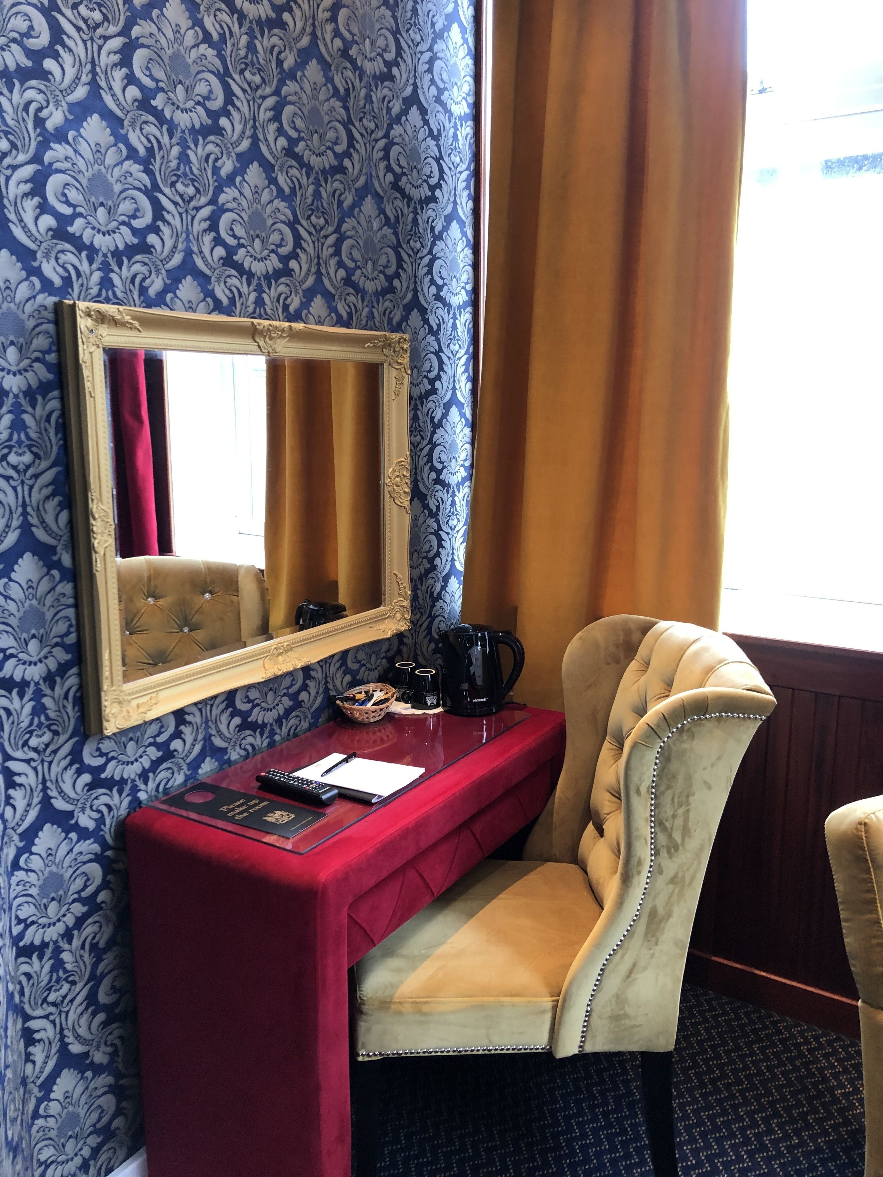 Una habitació amb un escriptori vermell, un butaqui beige, un mirall i un fons de pantalla amb dibuixos.