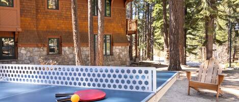 A ping pong table with balls, a wooden chair, and a building surrounded by trees.
