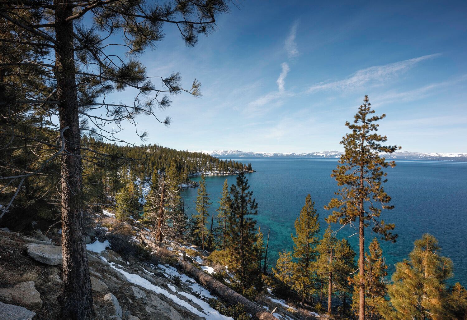 A mountainous landscape with a lake, trees, and snow-covered ground.