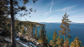 A mountainous landscape with a lake, trees, and snow-covered ground.