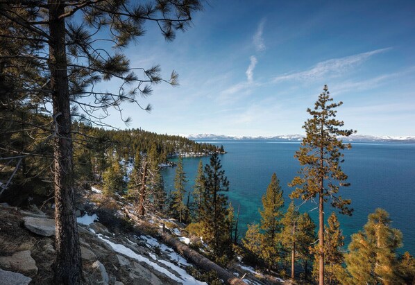 A mountainous landscape with a lake, trees, and snow-covered ground.