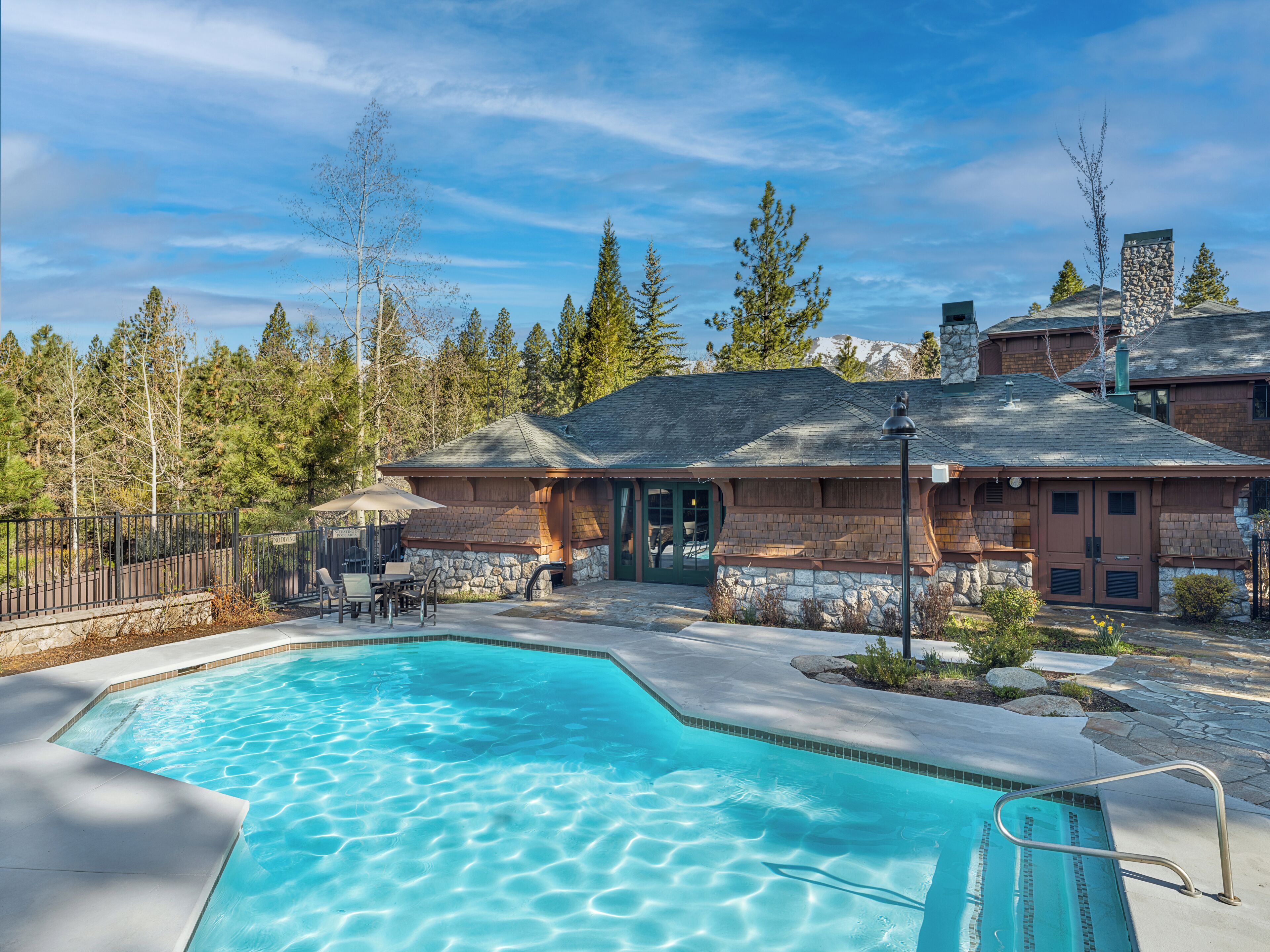 A pool area with a stone building, outdoor seating, and a view of trees and mountains.