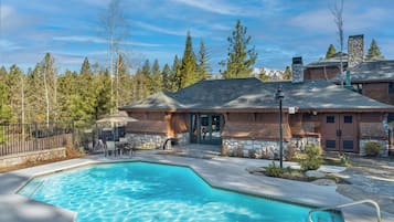 A pool area with a stone building, outdoor seating, and a view of trees and mountains.