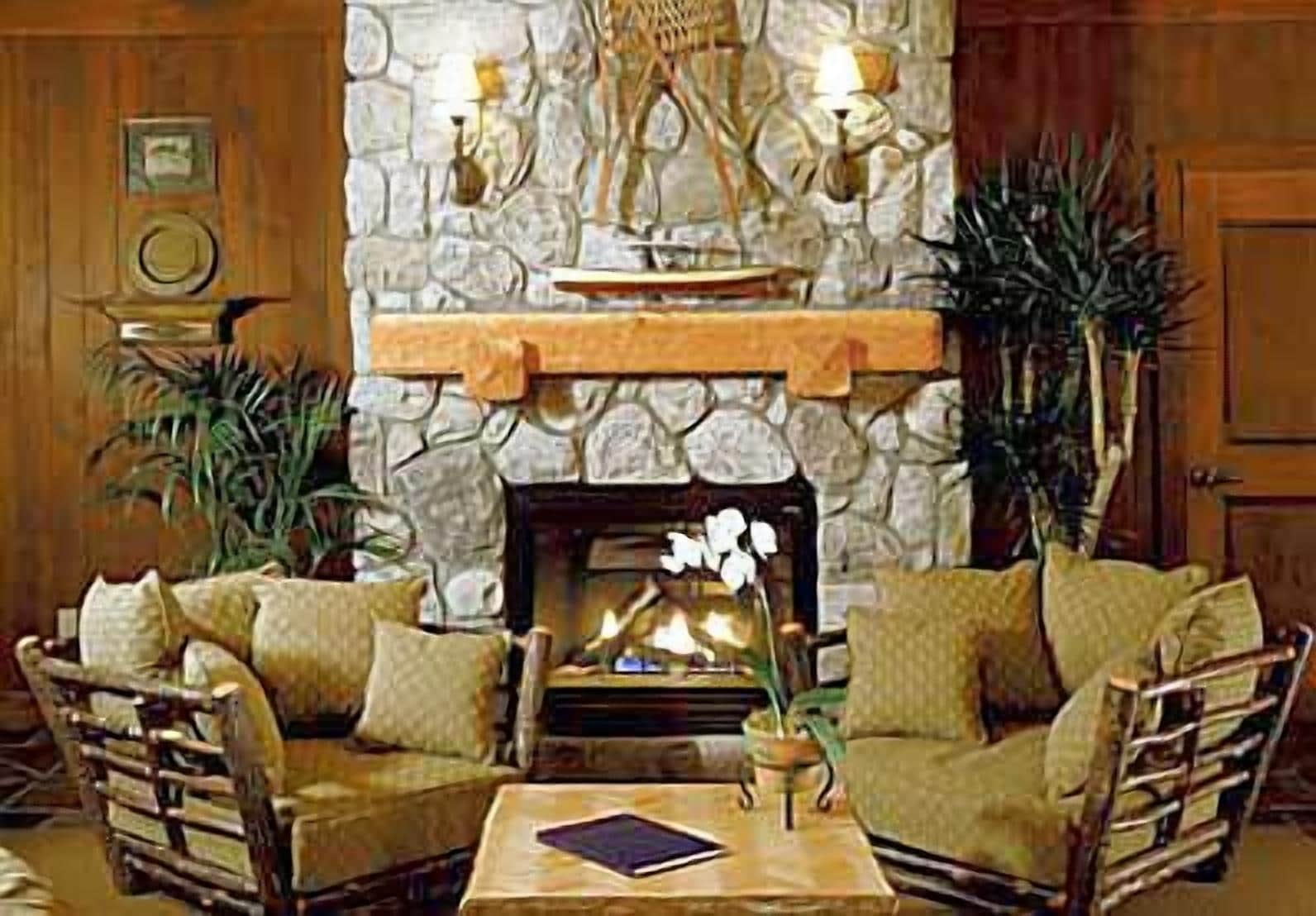 A cozy living room with a stone fireplace, two armchairs, a coffee table, and a bookshelf.