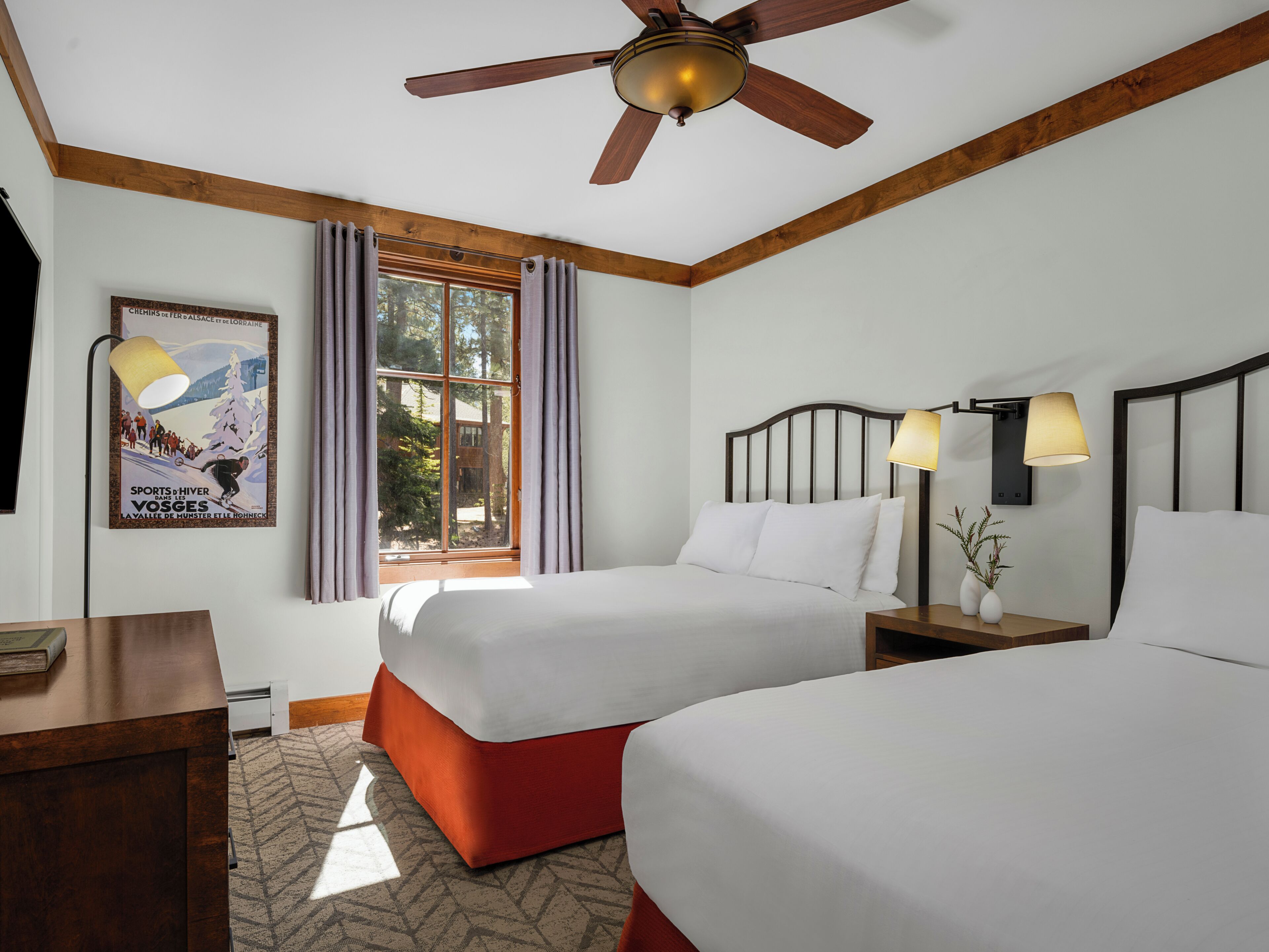 A hotel room with two beds, a ceiling fan, a window with curtains, a poster on the wall, and bedside lamps.