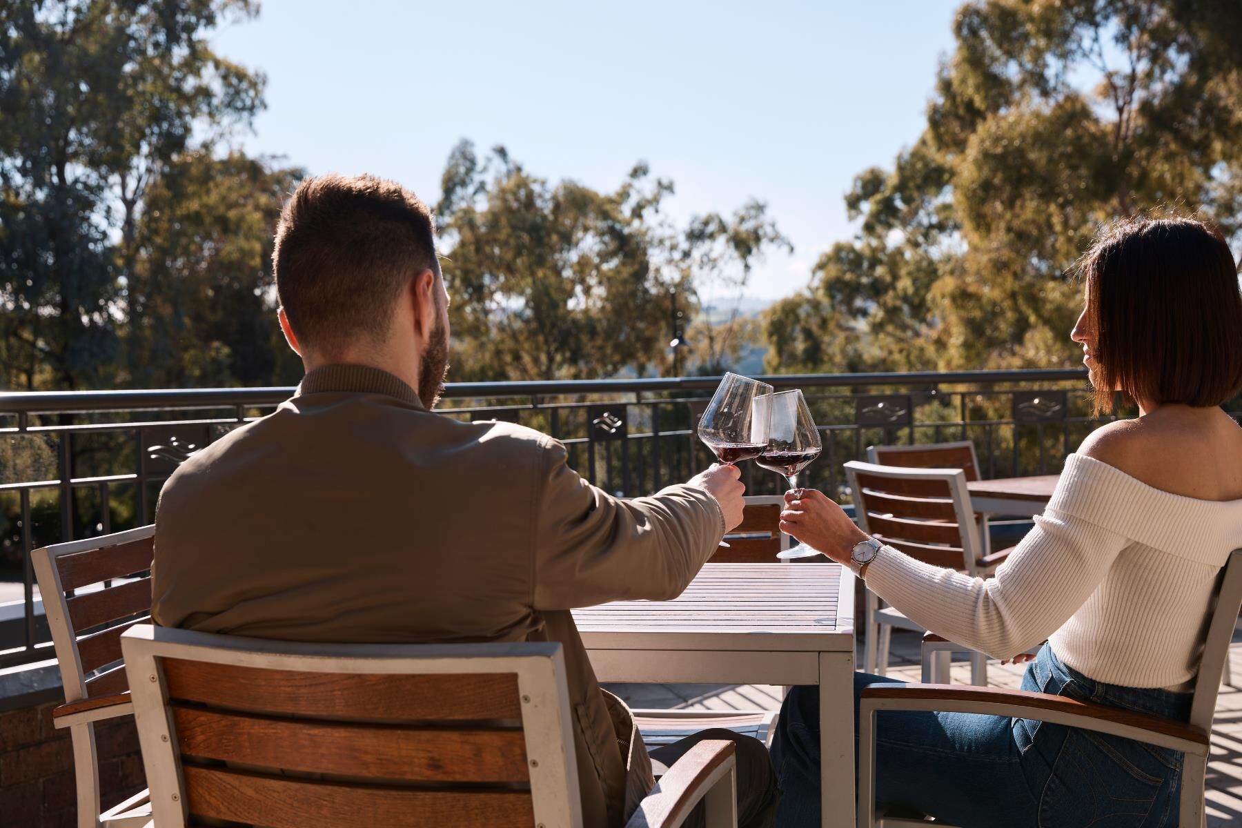 A couple seated at an outdoor table with a view of trees and a railing.