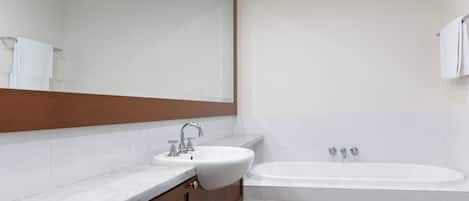 A bathroom with a sink, mirror, and bathtub.