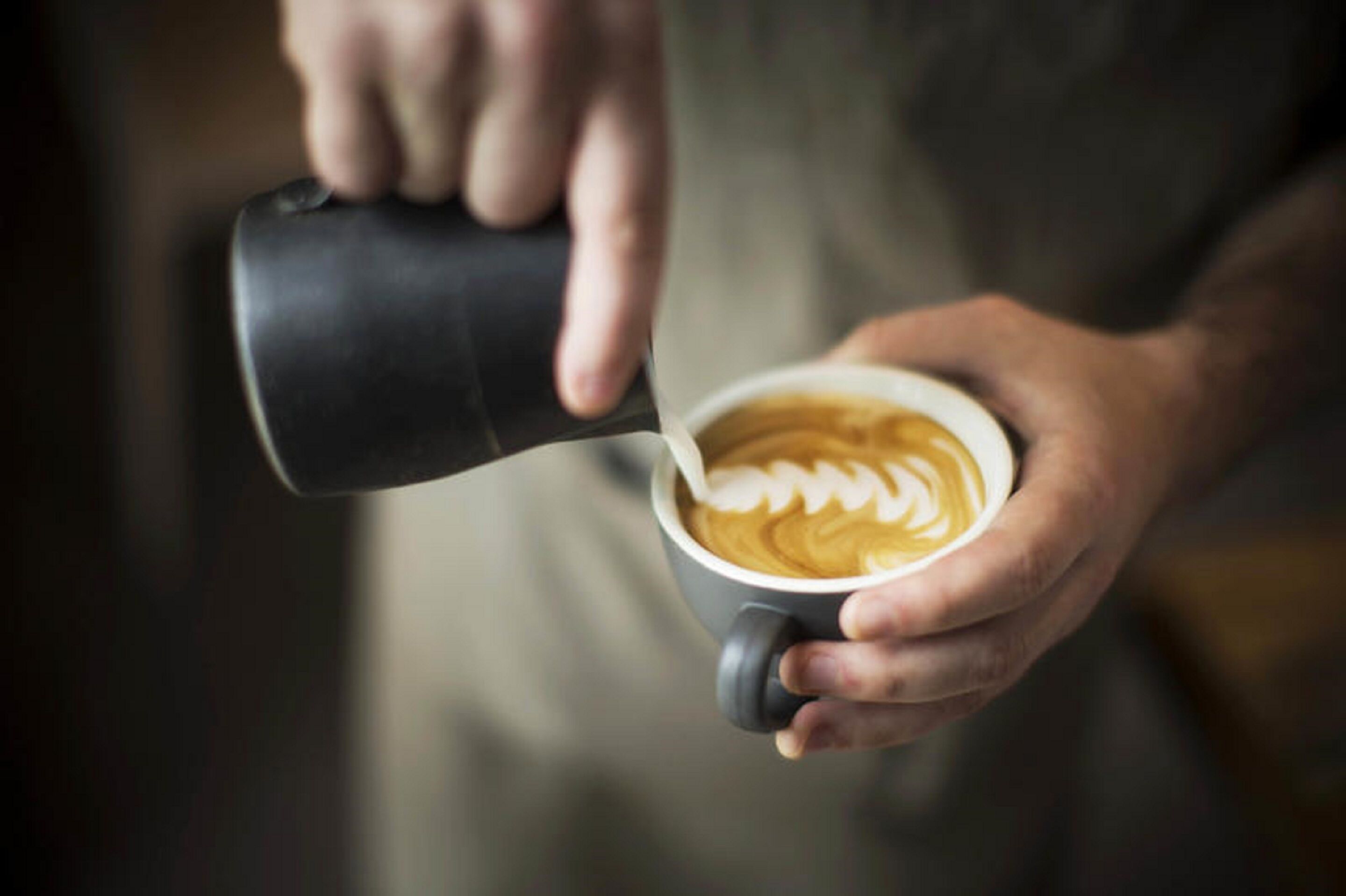 A person pouring milk into a cup of coffee with latte art.