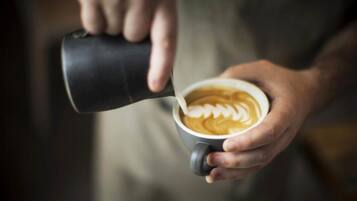 A person pouring milk into a cup of coffee with latte art.