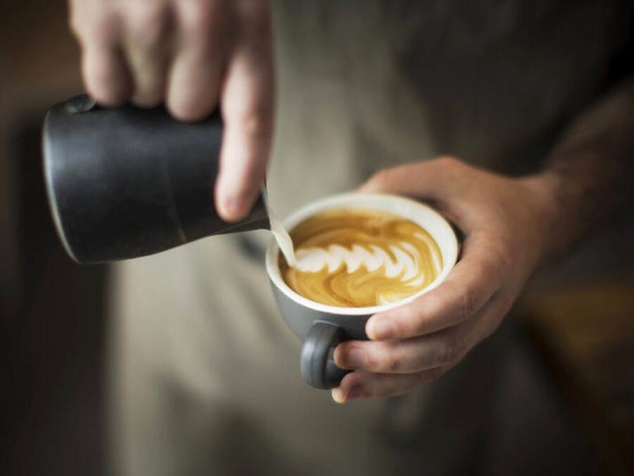 Una persona vertiendo leche en una taza de café con arte latte.
