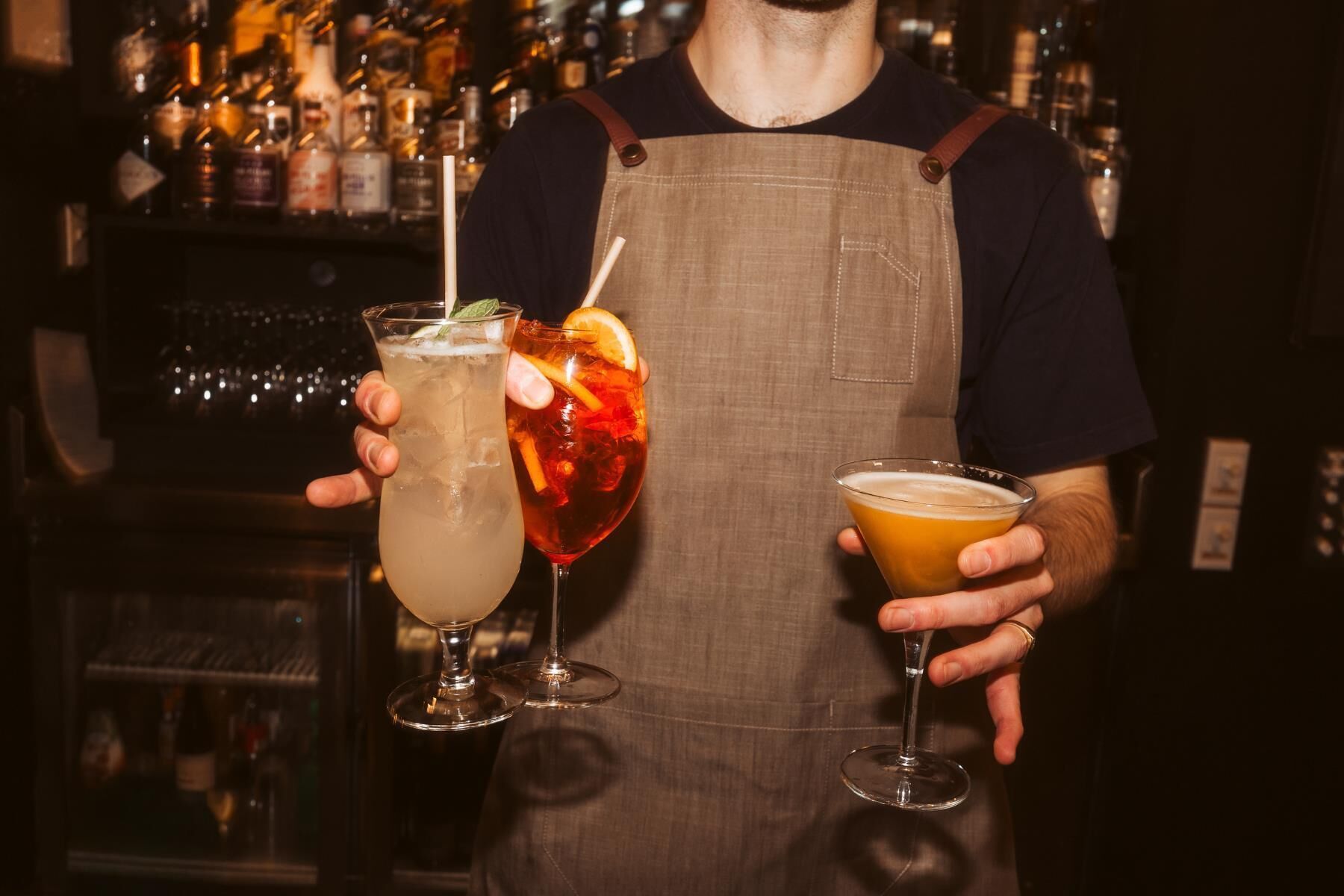 Un bartender sosteniendo tres bebidas distintas.