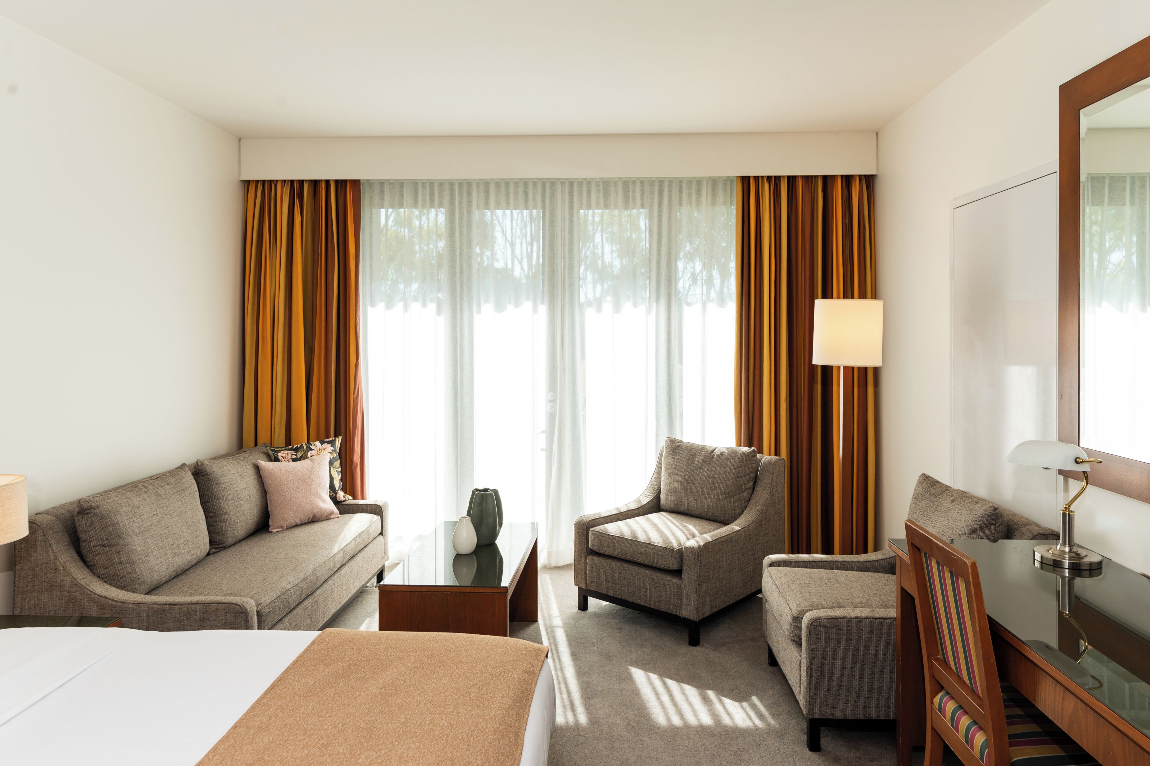 A hotel room with a bed, a sofa, a chair, a desk, and a lamp.