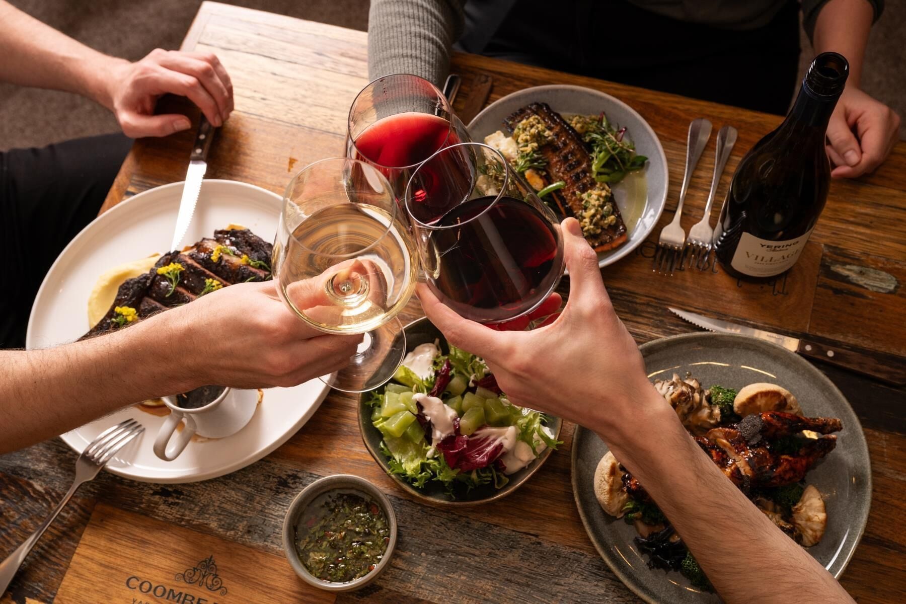 A dining table with plates of food, glasses of wine, and a bottle of wine.