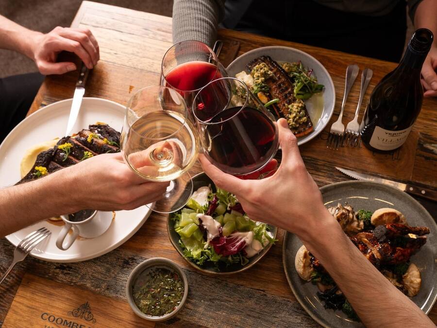 A dining table with plates of food, glasses of wine, and a bottle of wine.