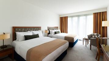 Habitación de hotel con dos camas, un escritorio, una silla y un ventanal con cortinas.