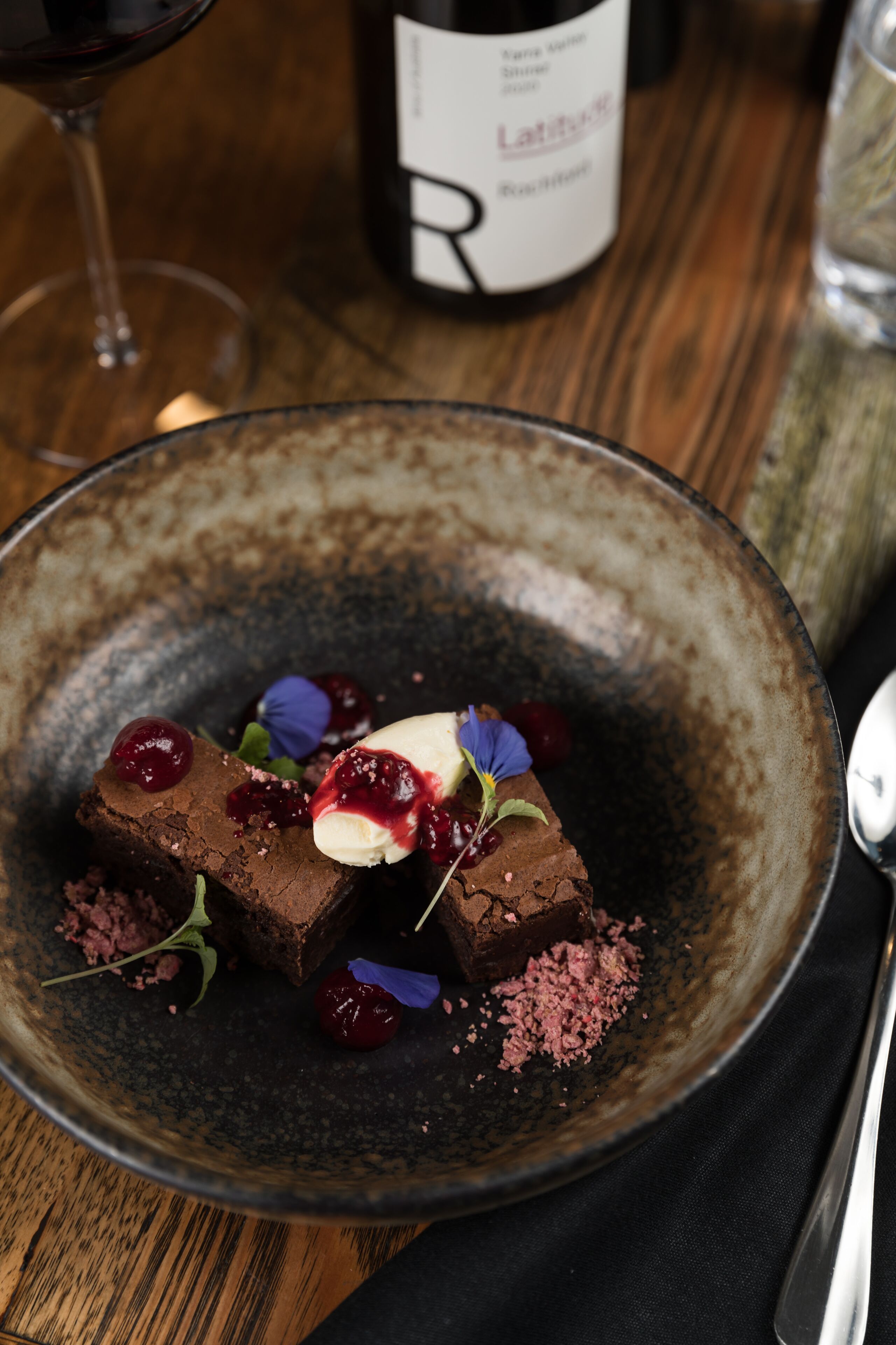 A dessert plate with chocolate pieces, cherries, and a dollop of cream on a rustic ceramic plate.