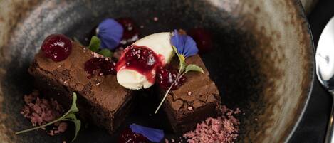 A dessert plate with chocolate pieces, cherries, and a dollop of cream on a rustic ceramic plate.