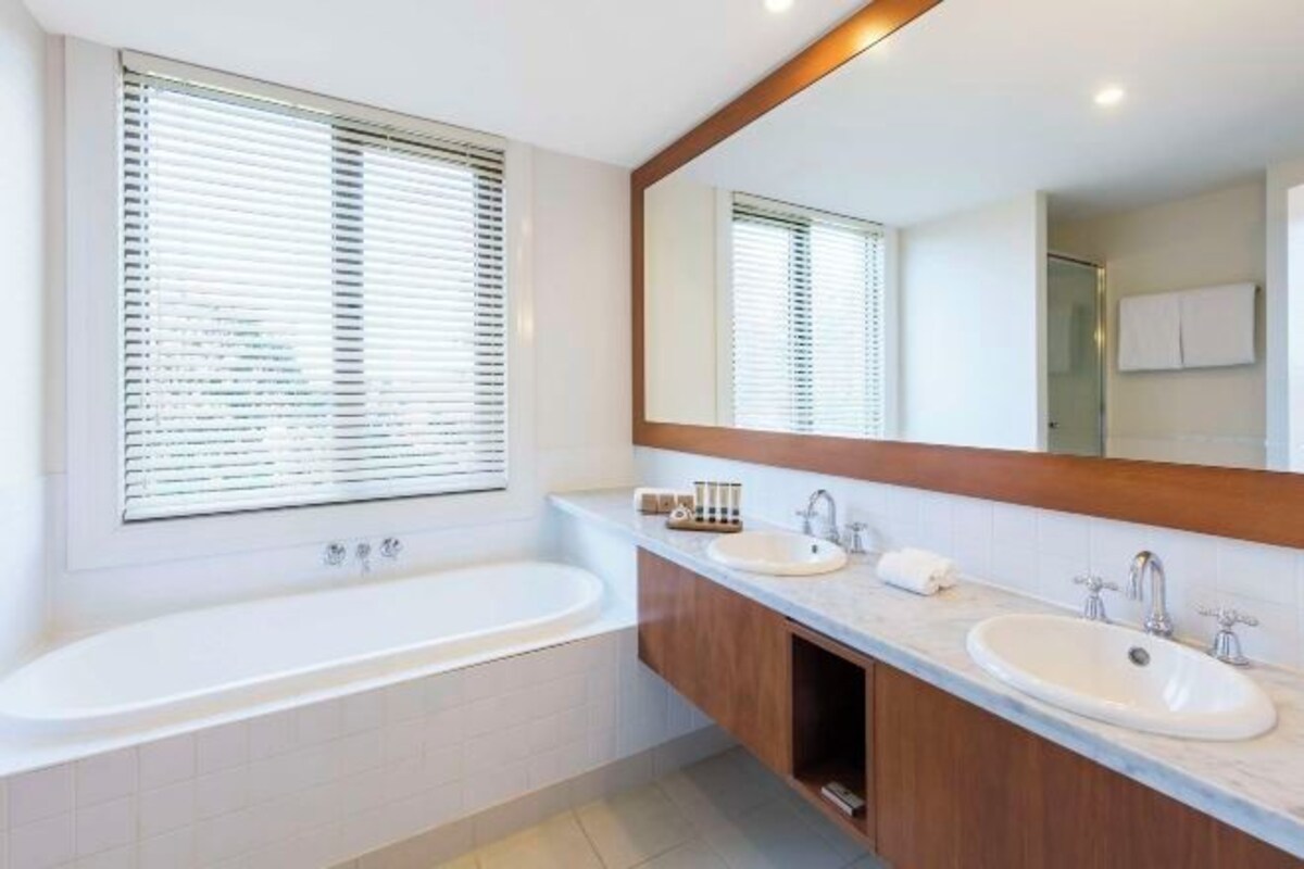 A modern bathroom with a bathtub, two sinks, and a large mirror.