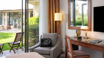 A hotel room with a sofa, a desk, a chair, a TV, a lamp, and a view of the outdoor area.