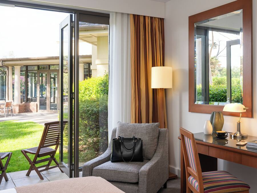 Habitación de hotel con sofá, escritorio, silla, televisor, lámpara y vista al área exterior.