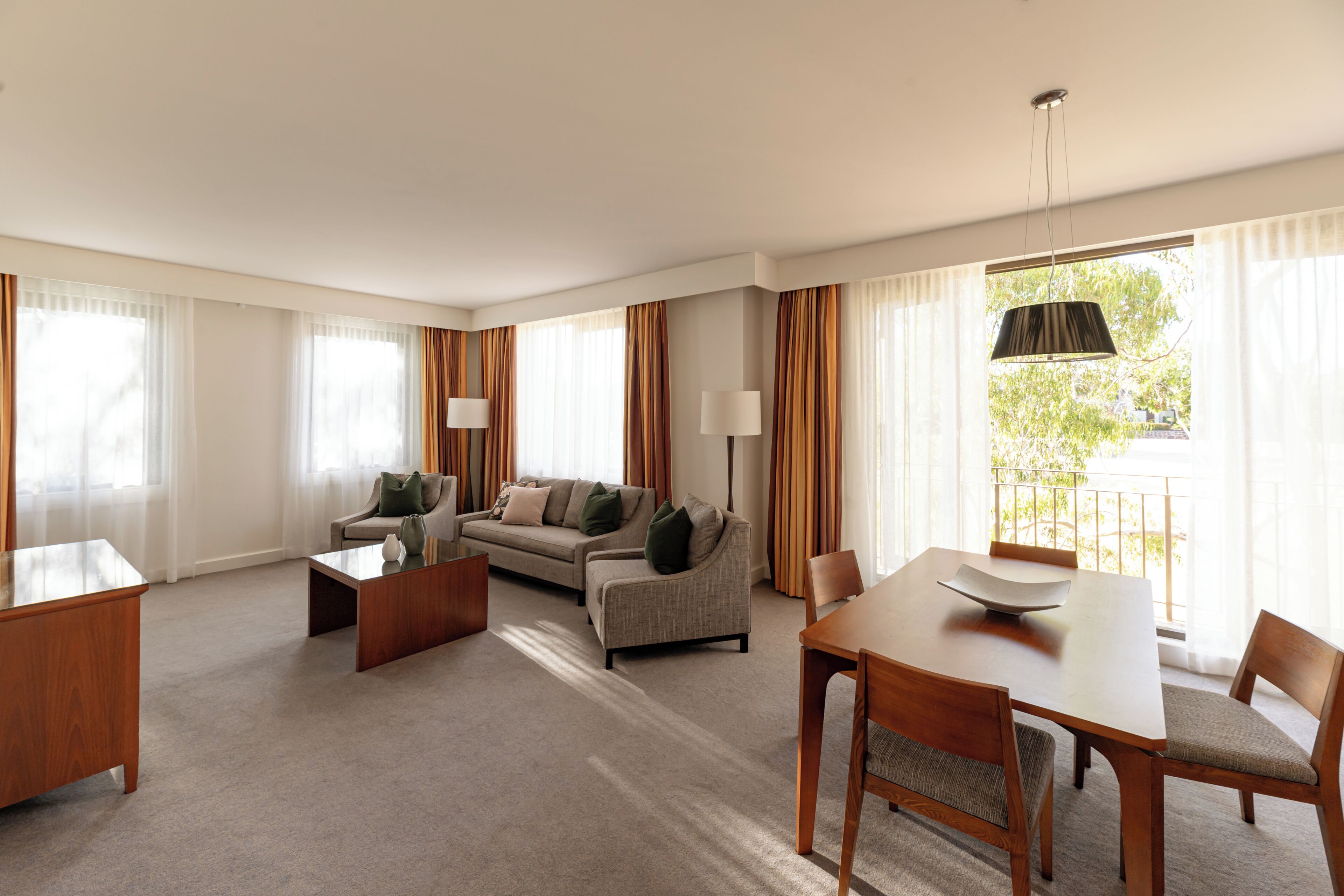 A hotel room with a sofa, a dining table, a coffee table, and a lamp.