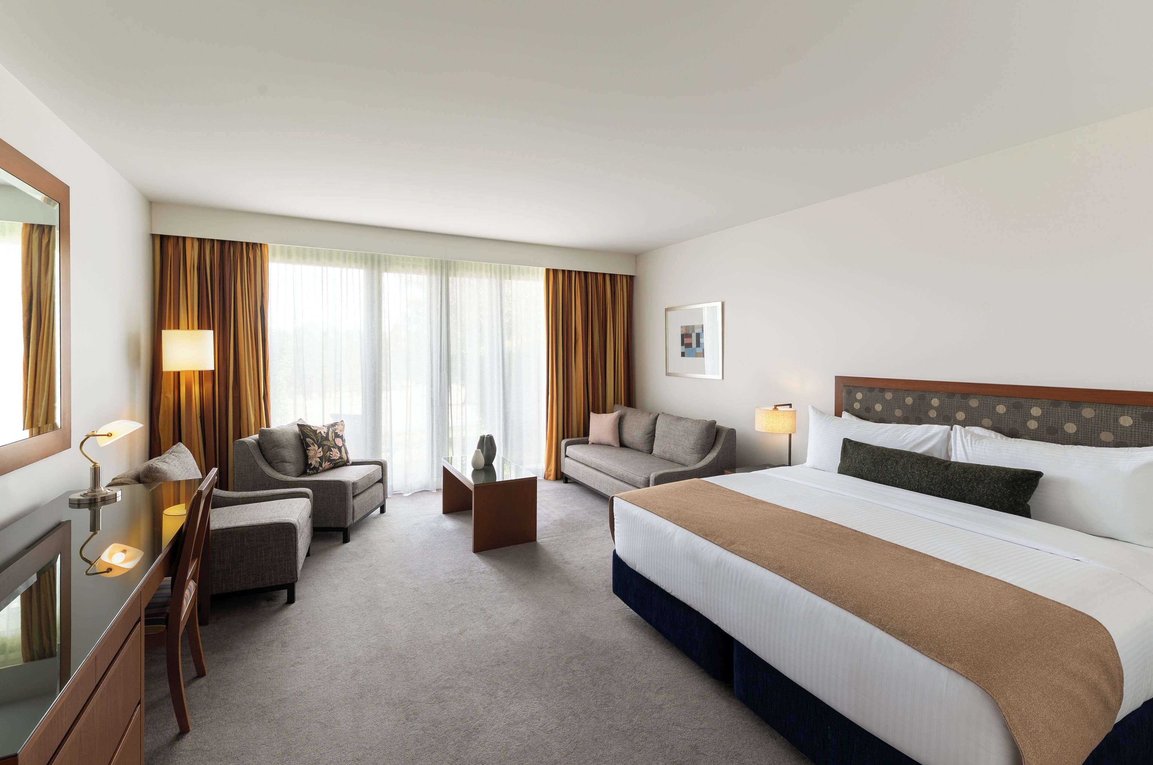 Una habitación de hotel con una cama, dos sofás, un escritorio y un espejo.