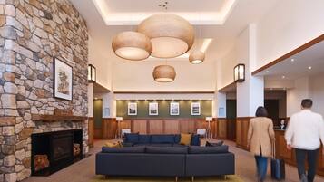 A modern lobby with a stone wall, a fireplace, a large dark sofa, and hanging wicker lamps.