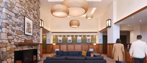 A modern lobby with a stone wall, a fireplace, a large dark sofa, and hanging wicker lamps.