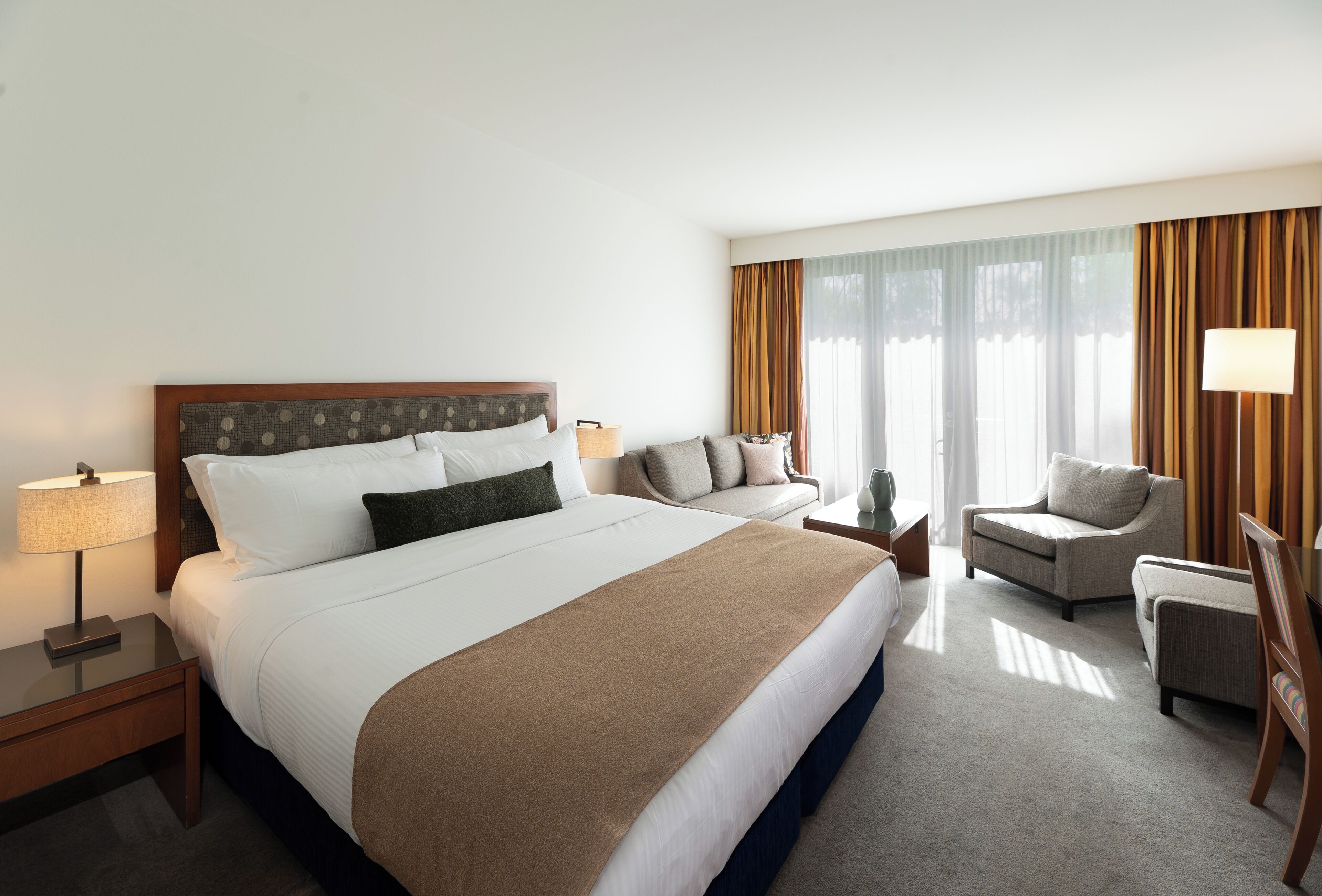 A hotel room with a large bed, a sofa, two armchairs, a lamp, and a nightstand.
