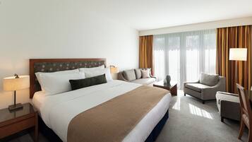 A hotel room with a large bed, a sofa, two armchairs, a lamp, and a nightstand.
