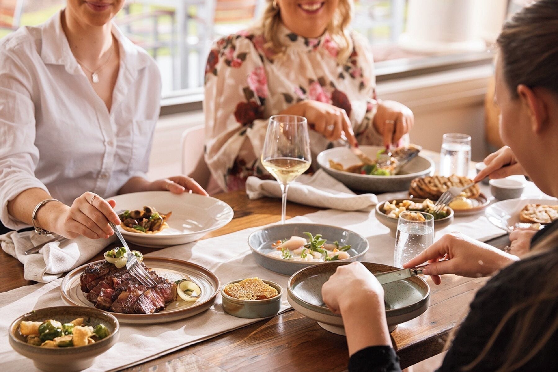 A group of people dining at a table with various dishes, including steak and vegetables.