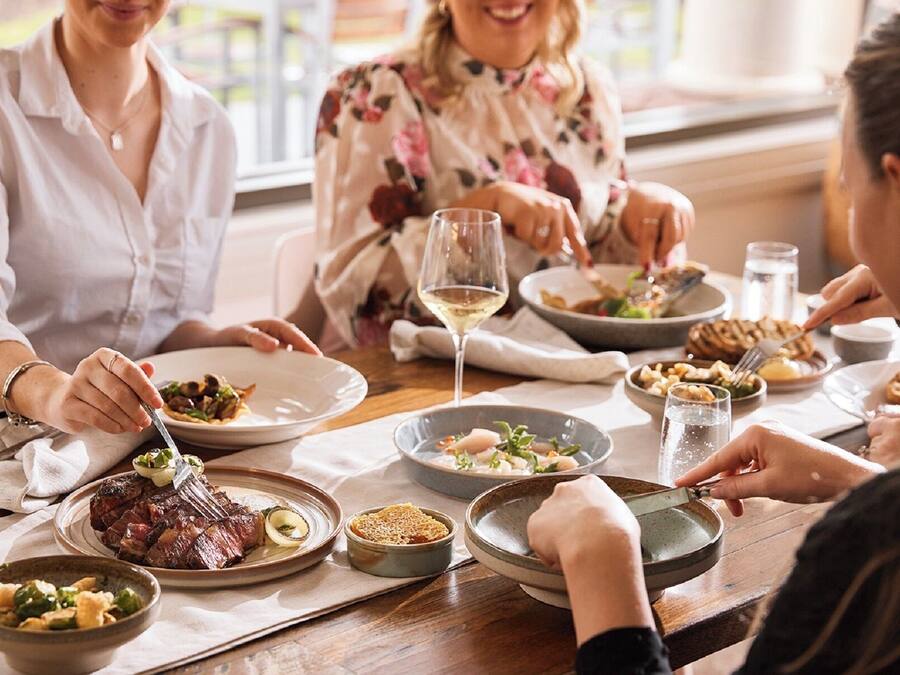 Eine Gruppe von Personen isst an einem Tisch mit verschiedenen Gerichten, darunter Steak und Gemüse.
