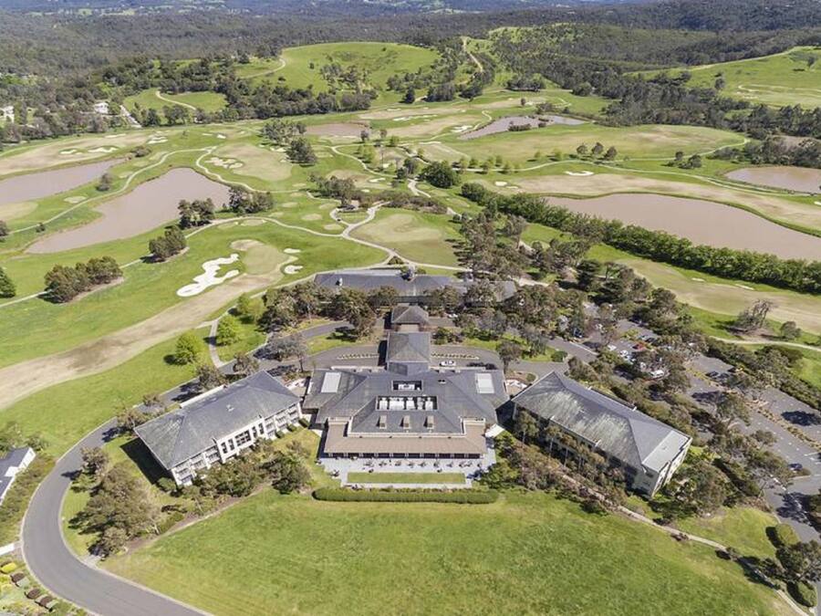 An aerial view of a golf course with a clubhouse, surrounded by lush greenery and ponds.