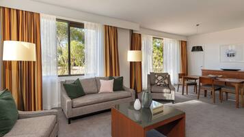 A hotel room with a sofa, armchair, dining table, and a lamp.
