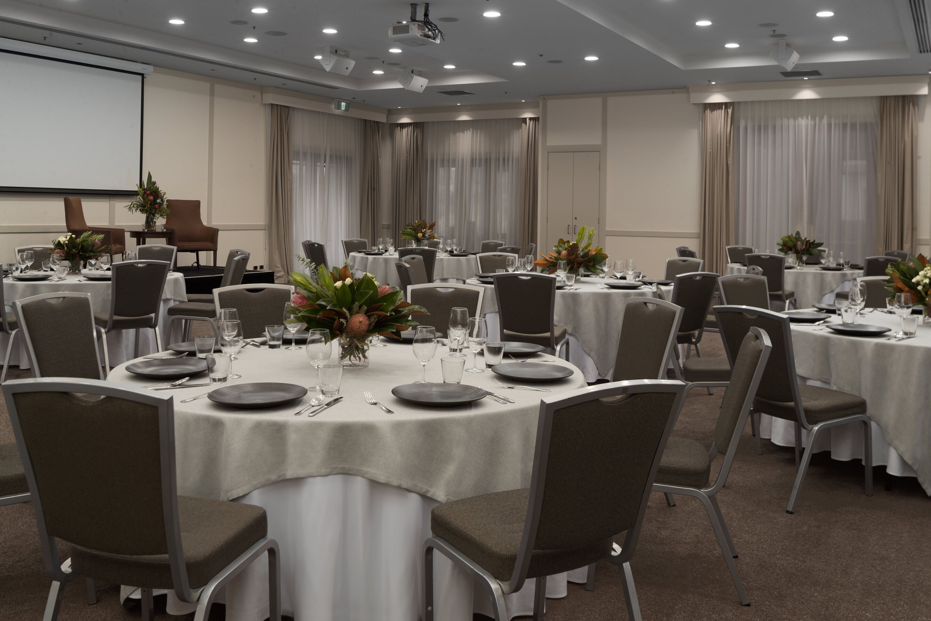 A conference room with round tables, chairs, and a projector screen.