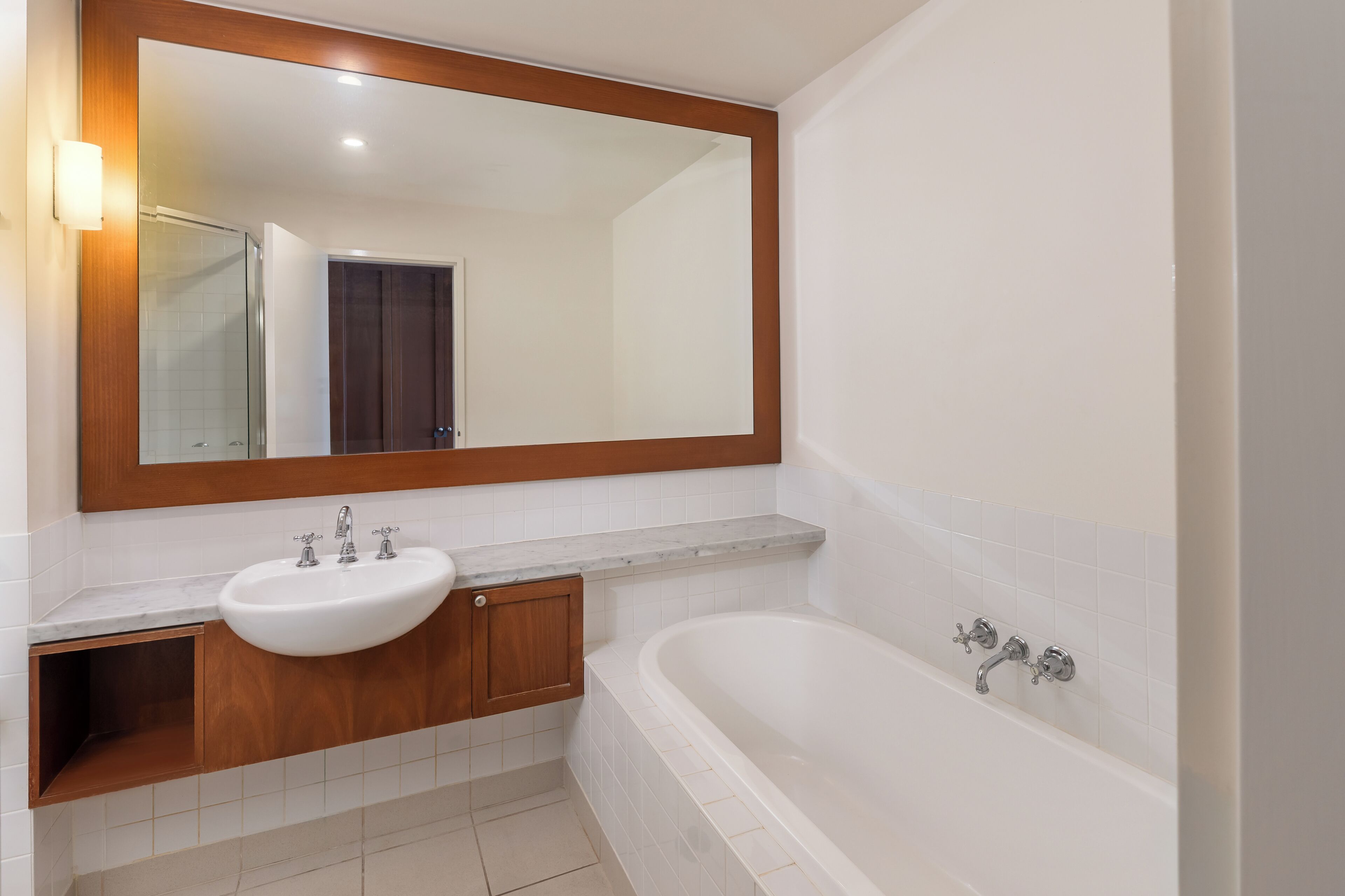 A bathroom with a white sink, a large mirror, a bathtub, and a wooden cabinet.