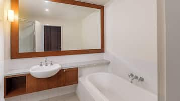 A bathroom with a white sink, a large mirror, a bathtub, and a wooden cabinet.
