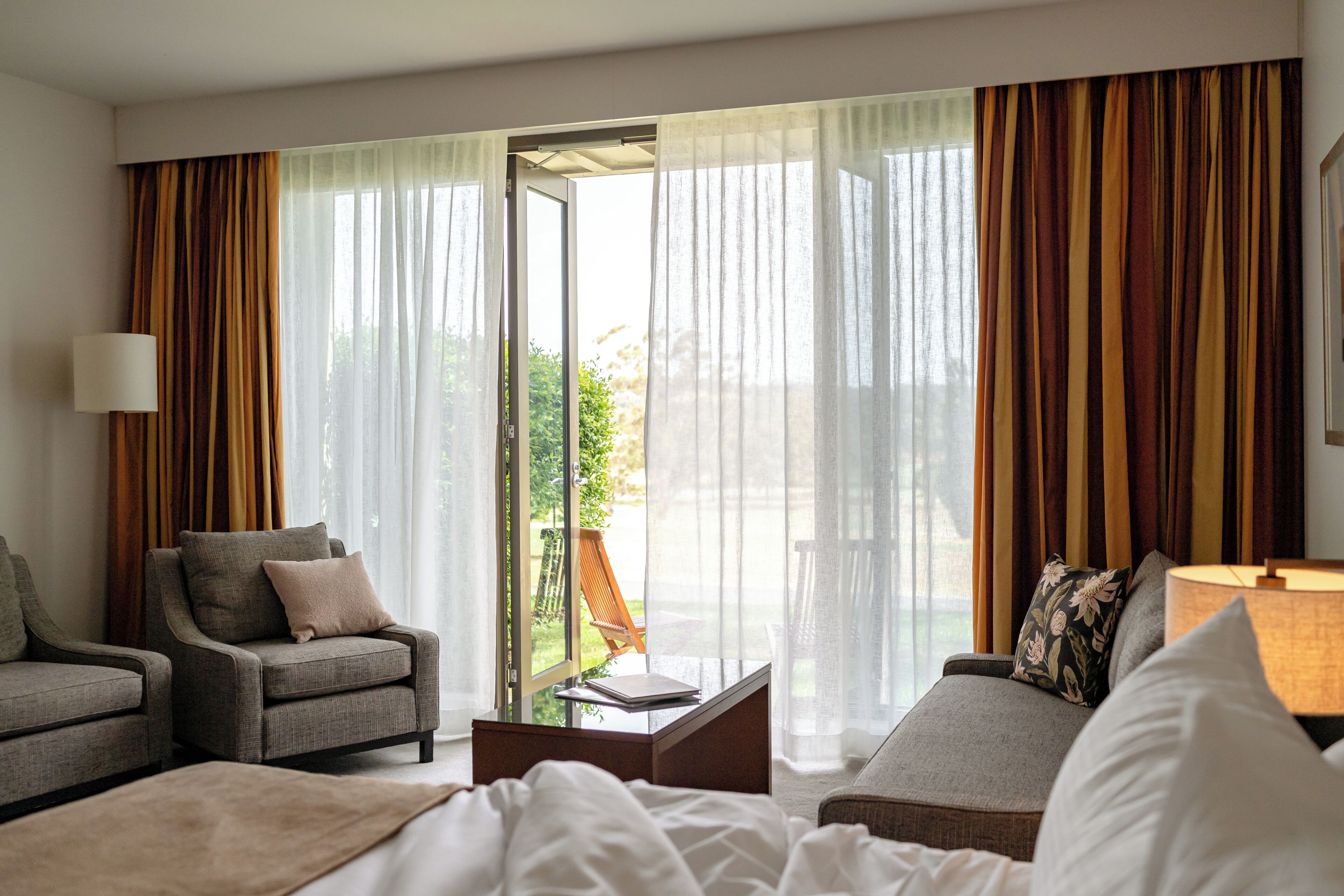 A hotel room with a bed, two armchairs, a sofa, a coffee table, and a lamp.