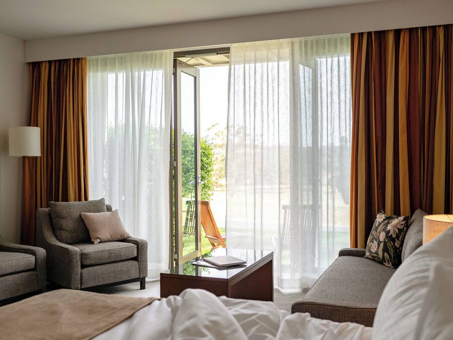 Quarto de hotel com uma cama, duas poltronas, um sofá, uma mesa de centro e um abajur.