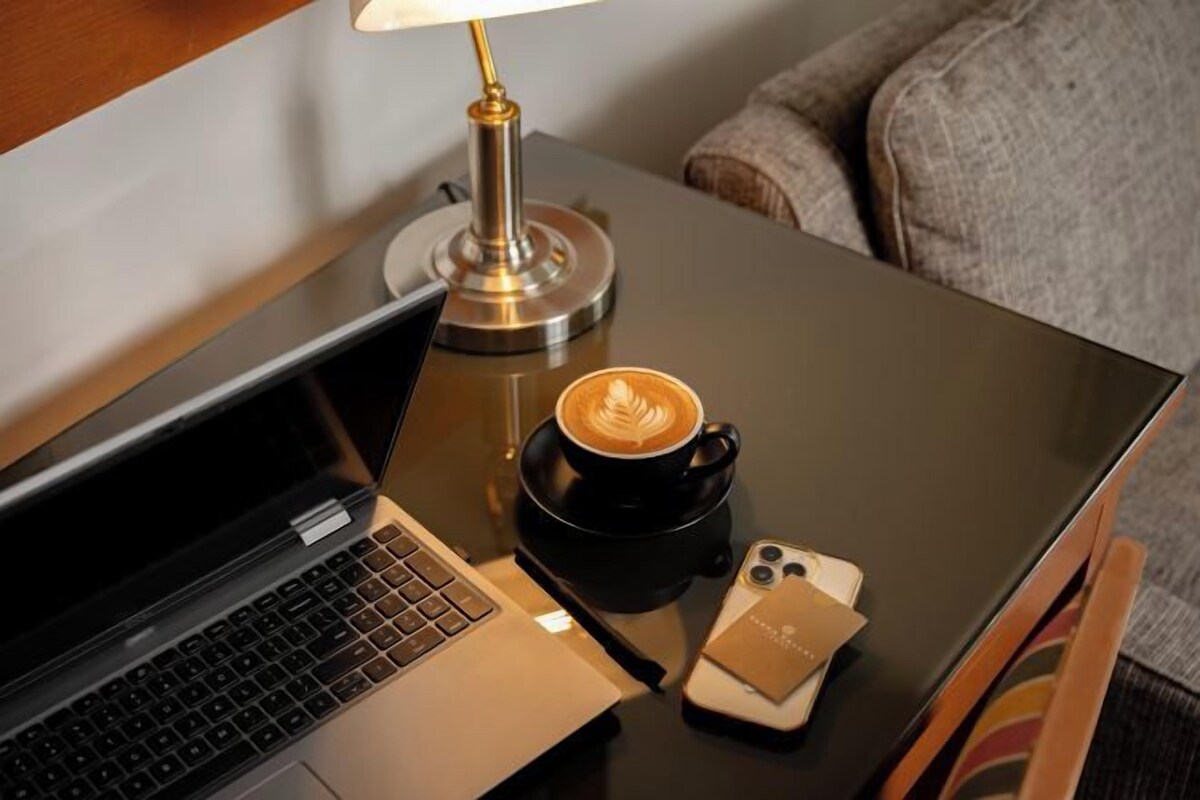 A laptop, a smartphone, a coffee cup, and a lamp on a table.