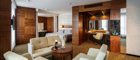 Habitación de hotel con cama, zona de estar con dos sillones, una mesita, baño con espejo y minibar.