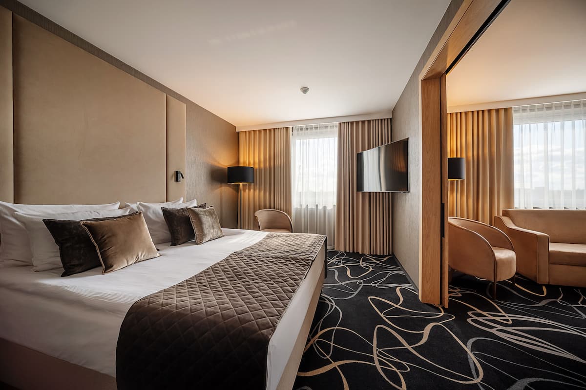 Een hotelkamer met een groot bed, twee fauteuils, een televisie en een bureau.