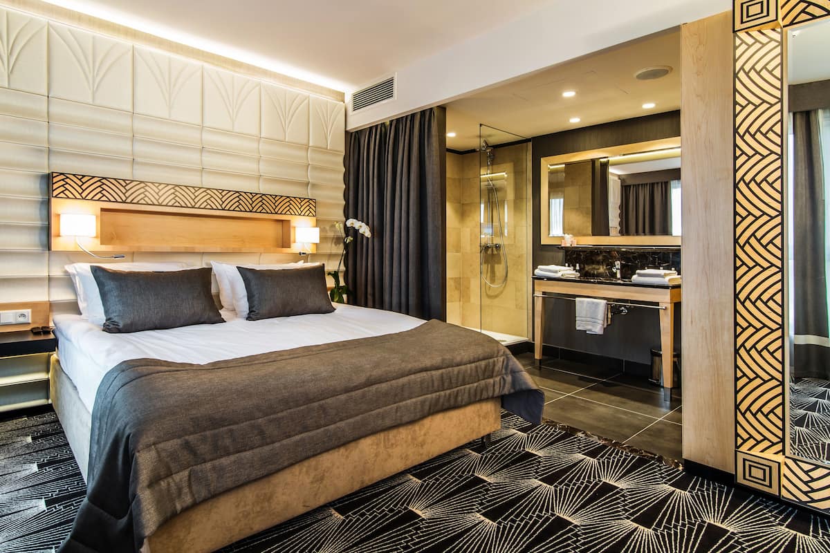 Een moderne hotelkamer met een groot bed, een badkamer met douche en een wastafel met spiegel.