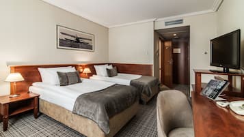 A hotel room with two beds, a desk with a TV, a chair, a lamp, and a painting on the wall.