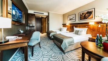 A hotel room with a large bed, a desk, a chair, a TV, and a bathroom visible through an open door.
