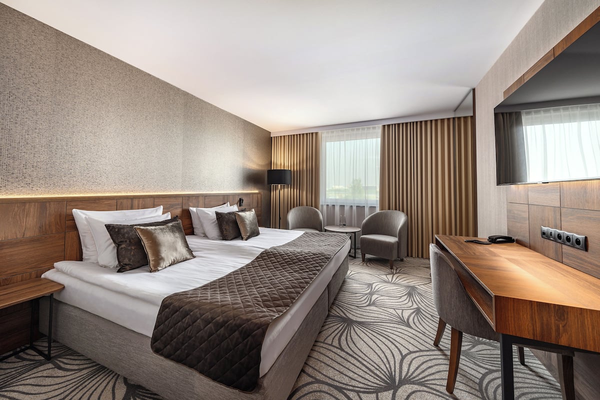 Een hotelkamer met een groot bed, een bureau, een stoel, een televisie en een raam met gordijnen.