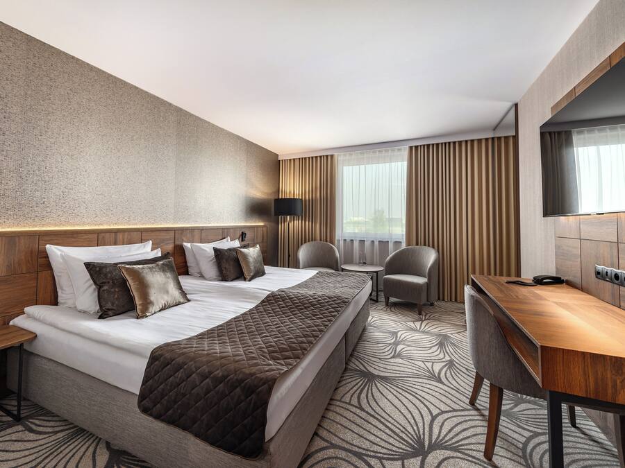 Une chambre d’hôtel avec un grand lit, un bureau, une chaise, une télévision et une fenêtre avec des rideaux.