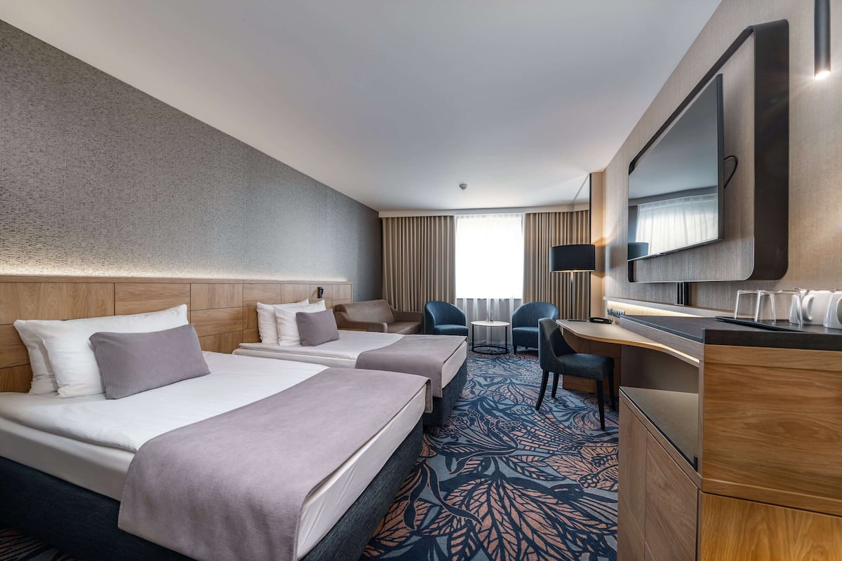 Een hotelkamer met twee bedden, een bureau, een stoel, een televisie en een raam met gordijnen.