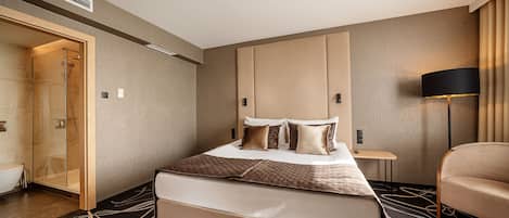 A modern hotel room with a large bed, a walk-in shower, a bedside table, and a lamp.