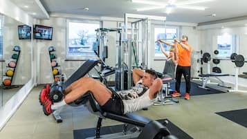 A gym with exercise equipment, a weight bench, and a person using a cable machine.